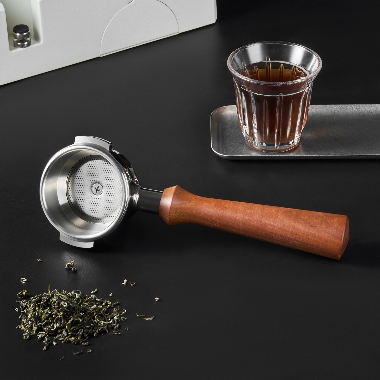 Tea portafilter beside loose leaves and a glass