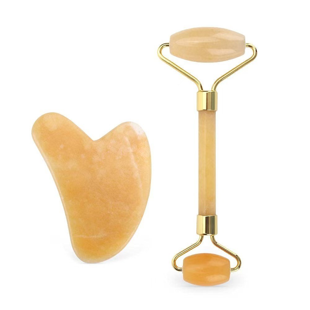 Yellow jade gua sha board and roller set on white background
