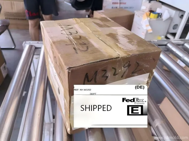 A shipping box with 'DE' and 'SHIPPED' labels on a factory line.