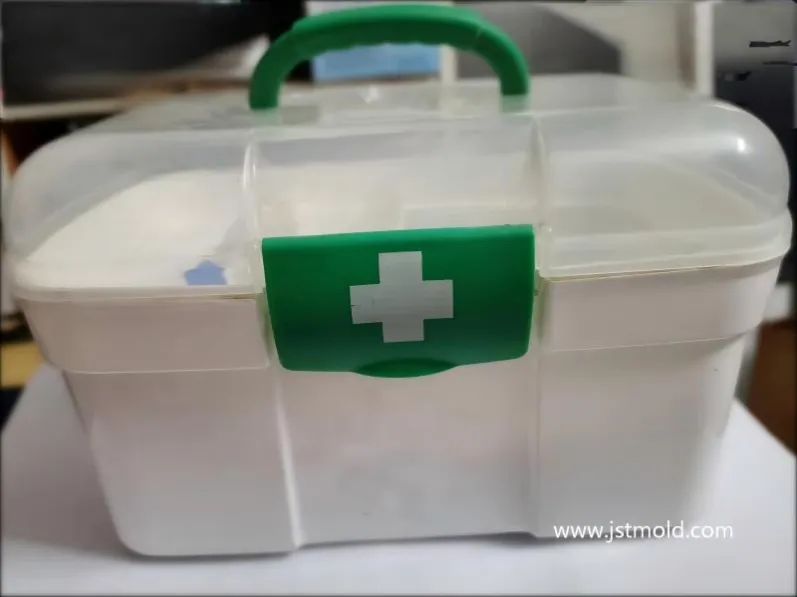 Close-up of a white plastic first aid box with a green locking latch featuring a white cross symbol.