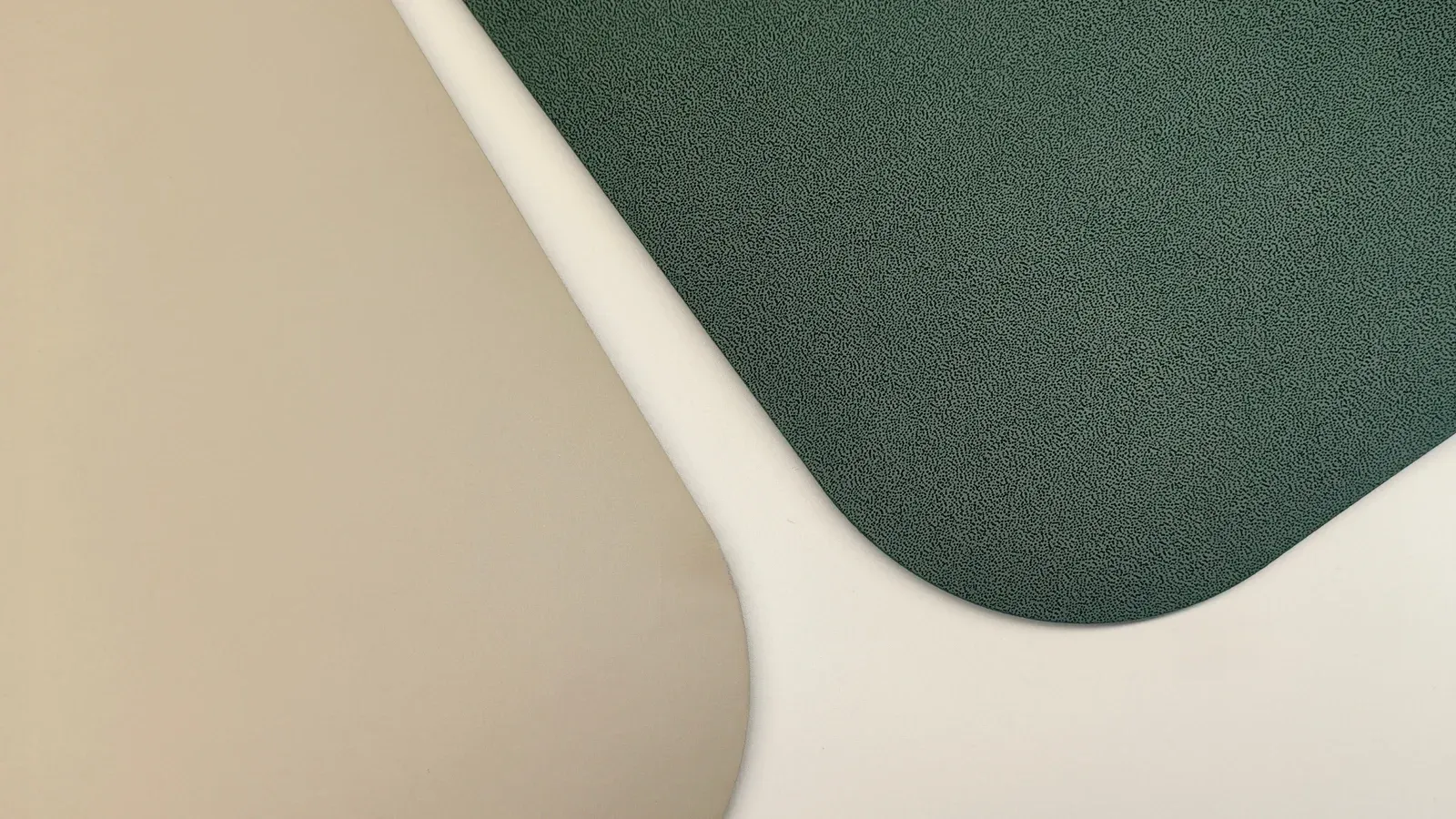 Two yoga mats overlapping at an angle on a pale surface, showing yoga mat surface texture: one beige face that is smooth and even, one dark green face in a fine dense grain, with a white mat edge between them