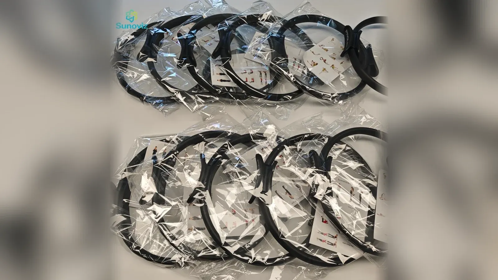 Black Pilates magic circle rings in clear plastic bags on a pale surface, each with a white exercise instruction card, two rows