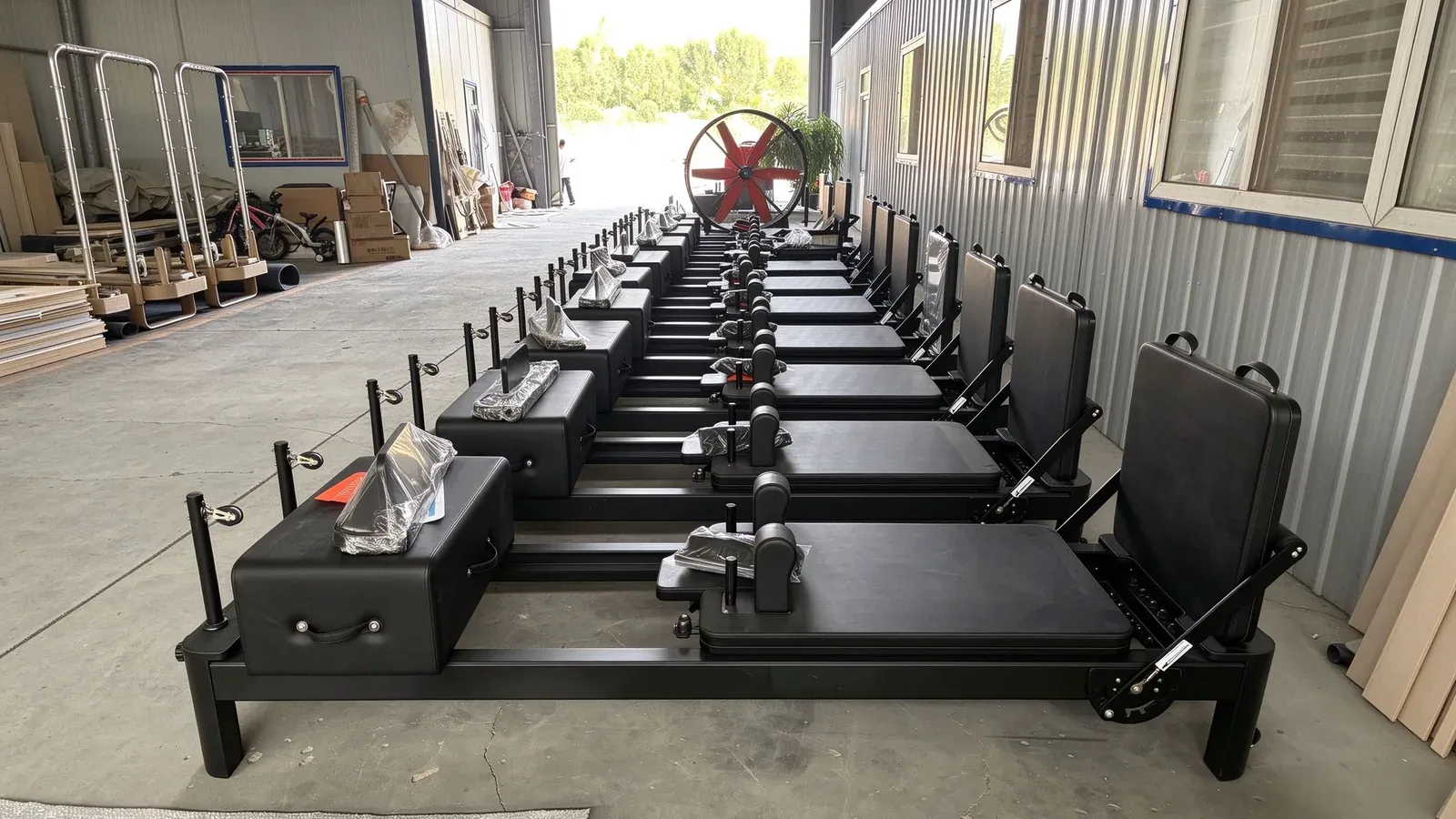 Long row of matte black classic Pilates reformers with protective film on their boxes in the workshop