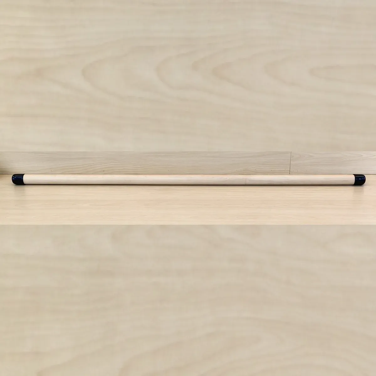 Maple wood Pilates training stick with a black anti-slip end cap at each end, on a light wood surface
