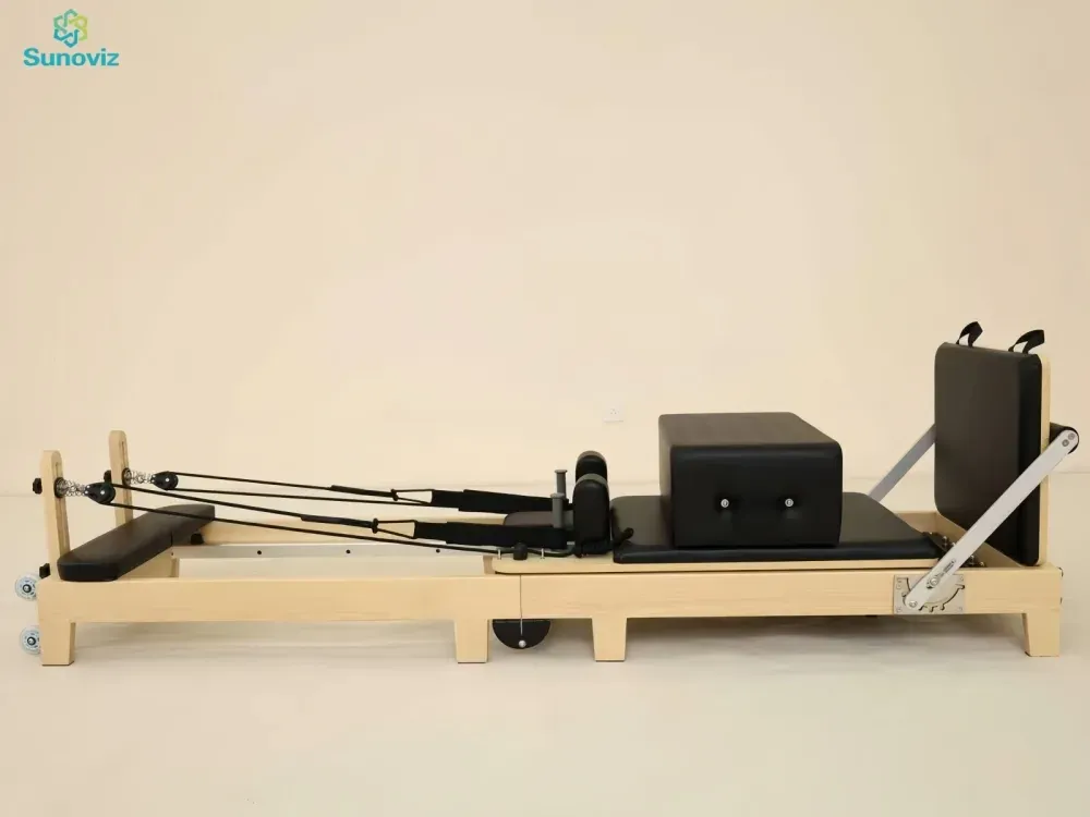 Maple Pilates reformer with black upholstery, box on the carriage and springs, standing on castors against a cream wall