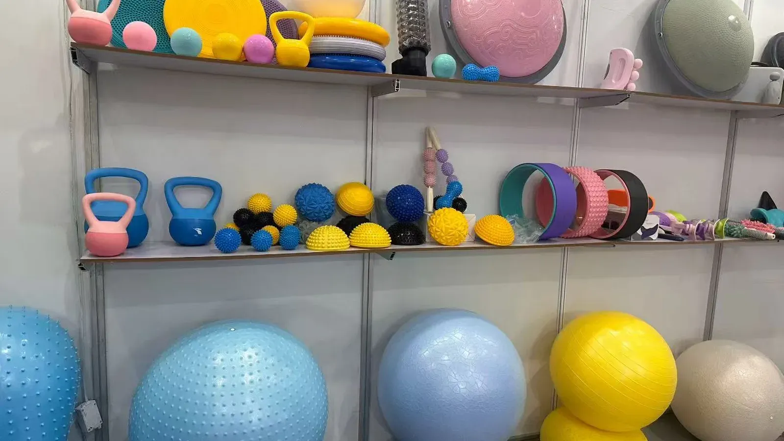 Shelf display of yoga balls, kettlebells, yoga wheels and foam rollers in assorted colors