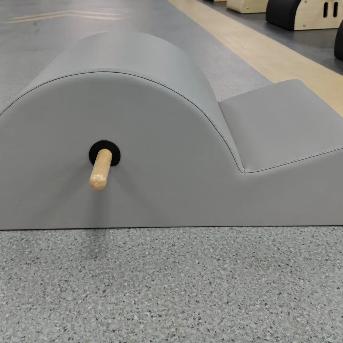 Three-quarter view of the grey Pilates spine corrector with a wooden bar projecting at the side