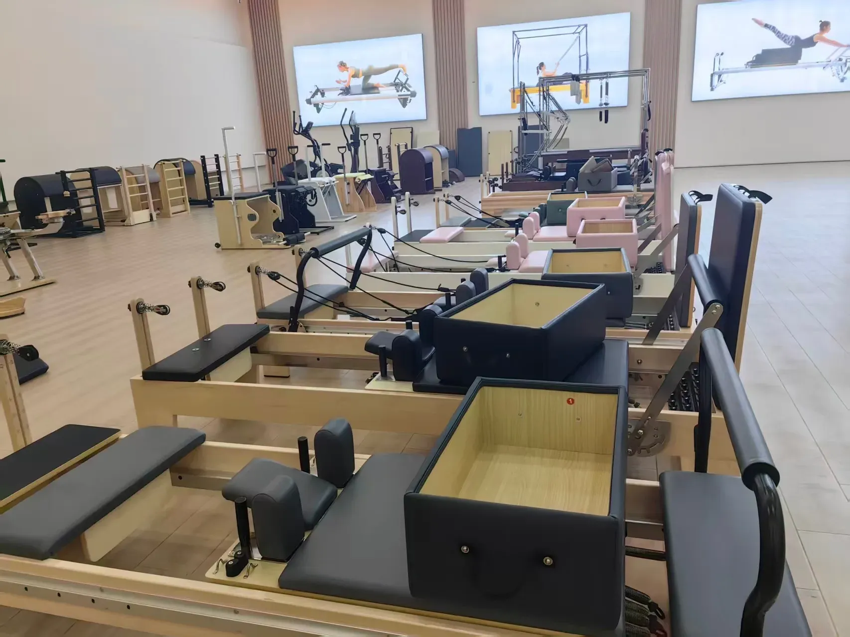 Pilates showroom with a row of Reformer units in light and pastel finishes, padded boxes and wall screens