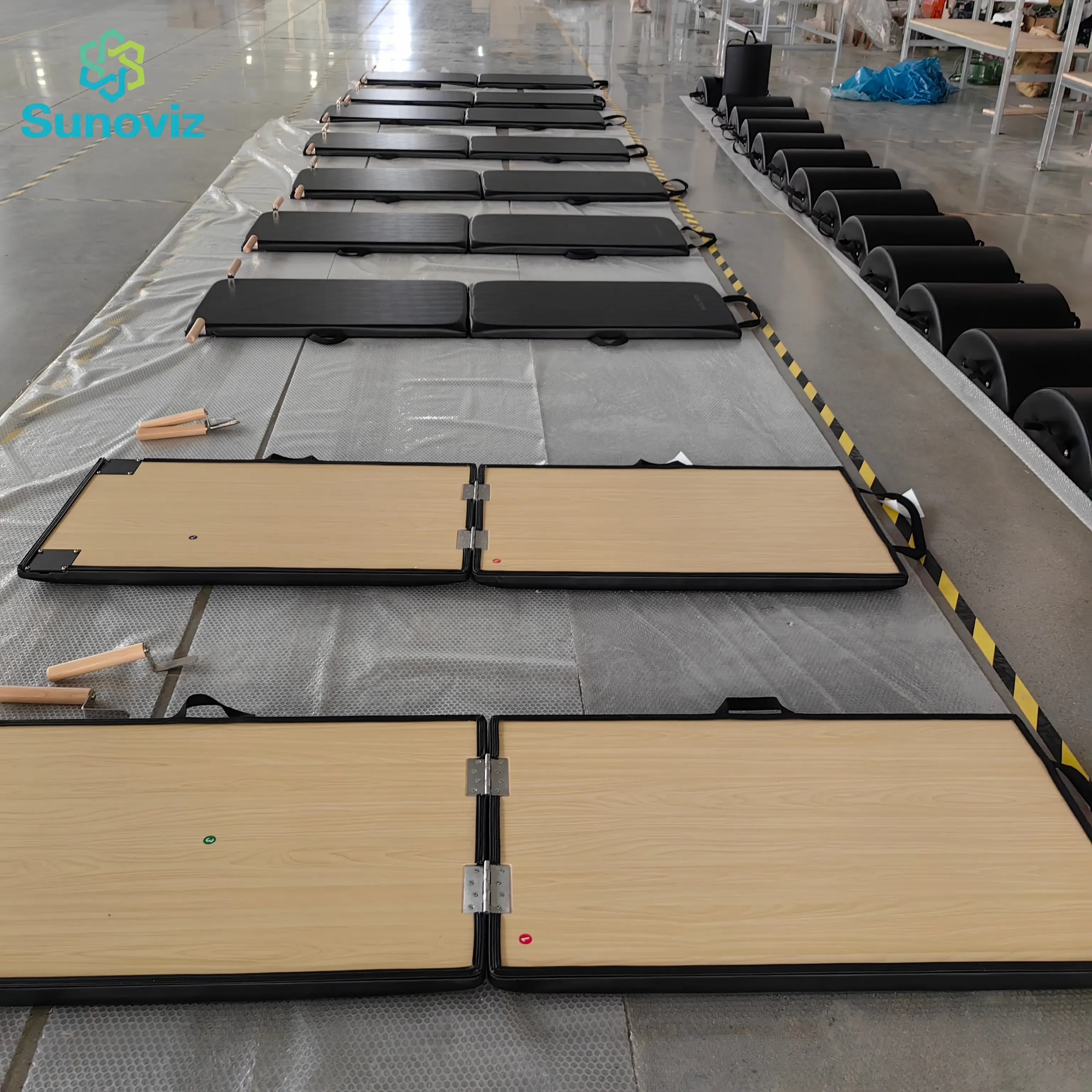 Classic Pilates folding mats and matching barrels laid out on protective sheeting during factory quality inspection