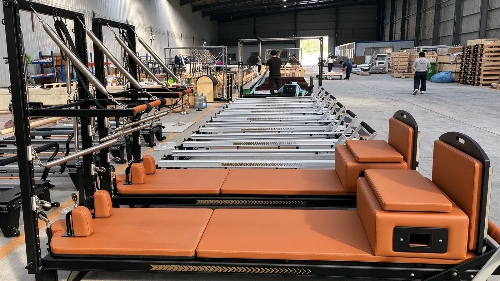 A row of bright orange-upholstered Pilates reformers with black half towers on a workshop floor