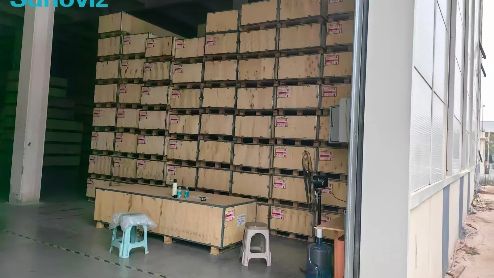 Warehouse interior filled with a wall of pale wooden export crates stacked on pallets, each crate labelled, with a long crate used as a work table in front