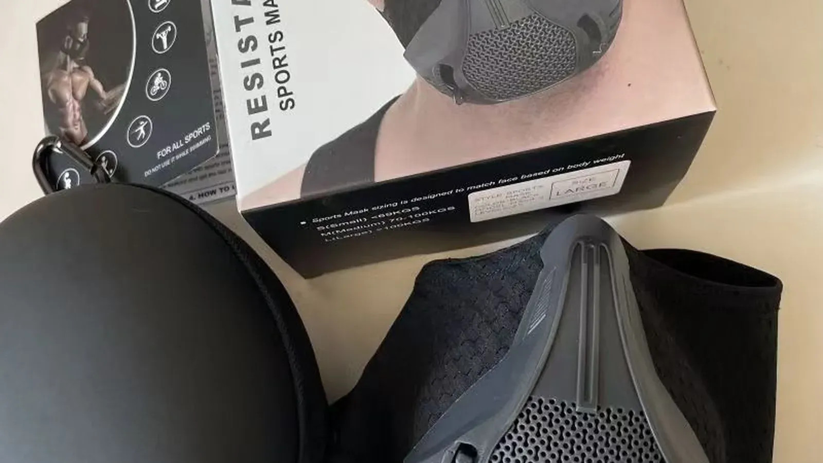 A black resistance sports training mask with its printed colour box and a black zippered carrying case beside it