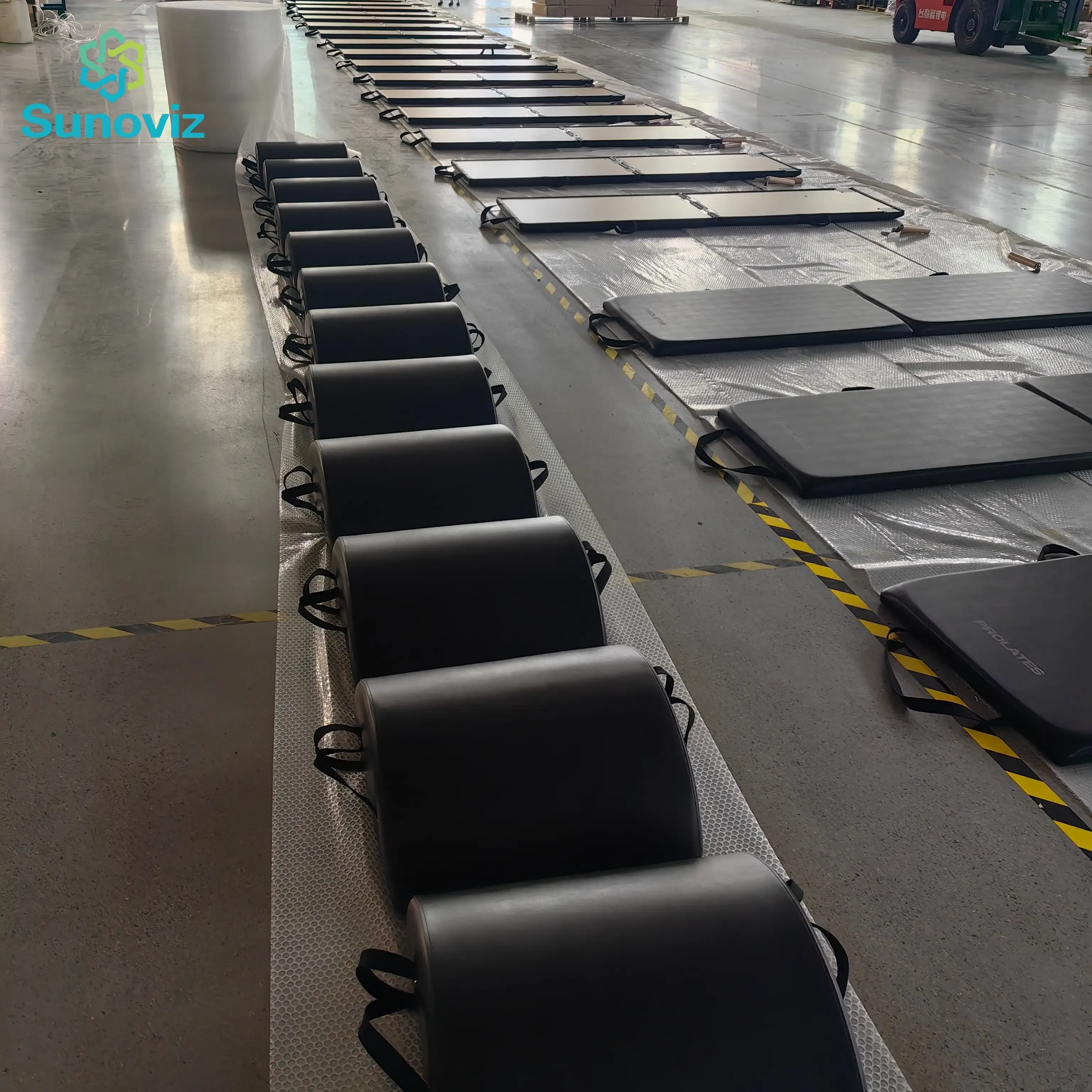 Rows of finished black Pilates small barrels with carry handles on protective sheeting in the factory