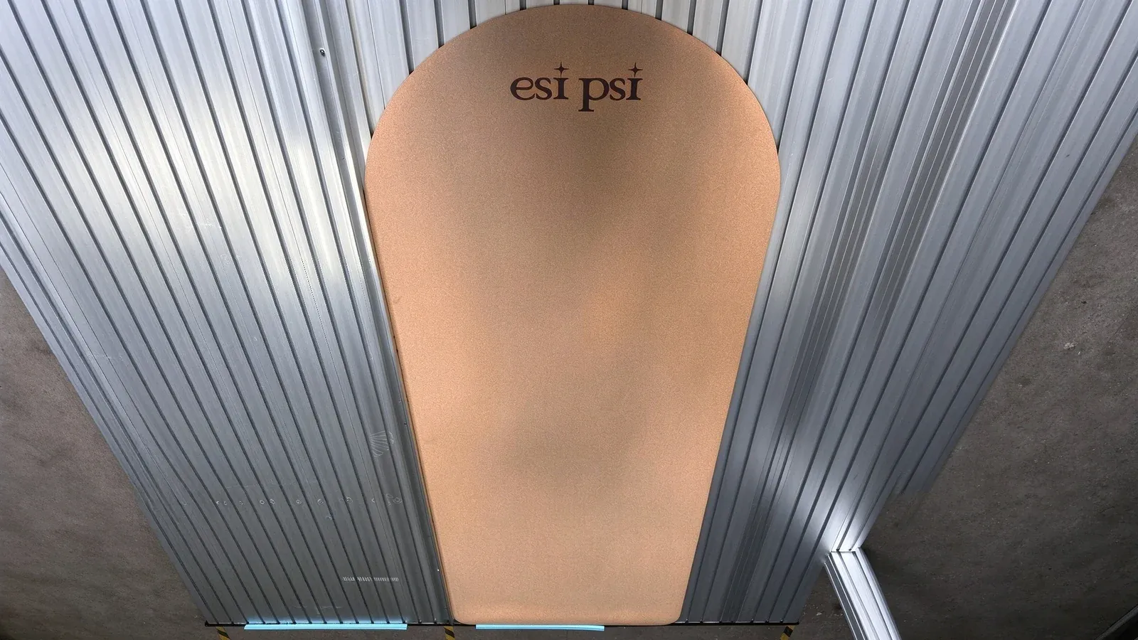 A natural cork yoga mat with an arched end and a laser-engraved logo, lying on a slatted metal worktable in the workshop