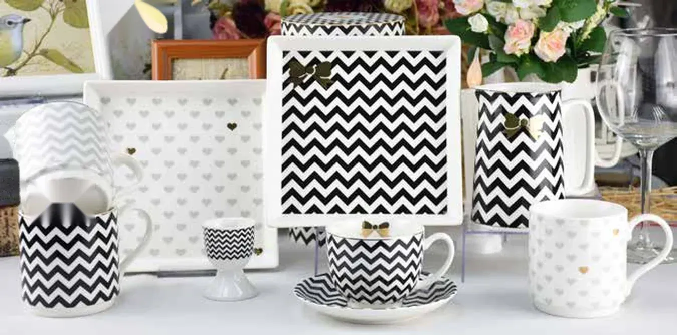 Black-and-white chevron and heart patterned ceramic gift collection: square trays, a chevron mug, a chevron teacup and saucer, a heart-print cup and a footed egg cup