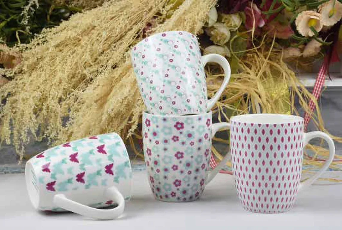 Four ceramic mugs printed with small florals, dots and butterflies in pink and mint, one lying on its side