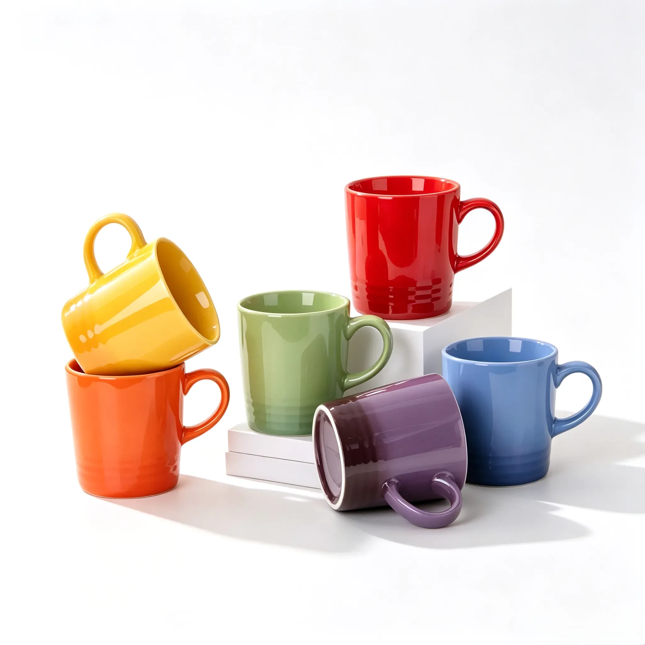 Six glossy ceramic mugs in red, orange, yellow, green, blue and purple arranged on white blocks