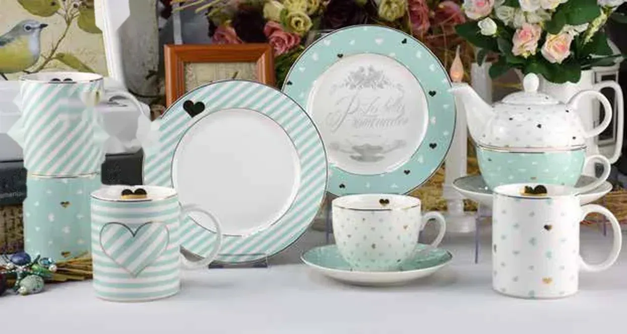 Mint green and white striped ceramic pieces with heart motifs: a teacup and saucer, white dotted heart-print cups, a teapot, dessert plates and stacked striped pieces