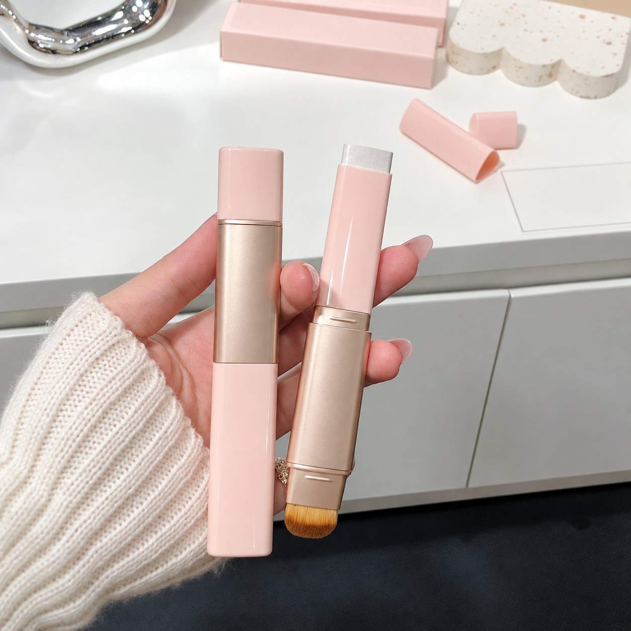 Closed and open color-changing foundation sticks held in hand, showing the sponge tip and flat blending brush
