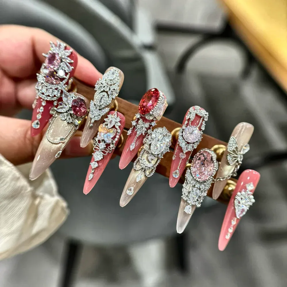 Detail view of 3D bow, sculpted flower and faceted crystal on coral pink and champagne long stiletto nails