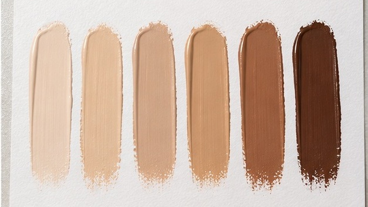 Concealer swatch applied to skin and checked against a shade card beside a neutral surface