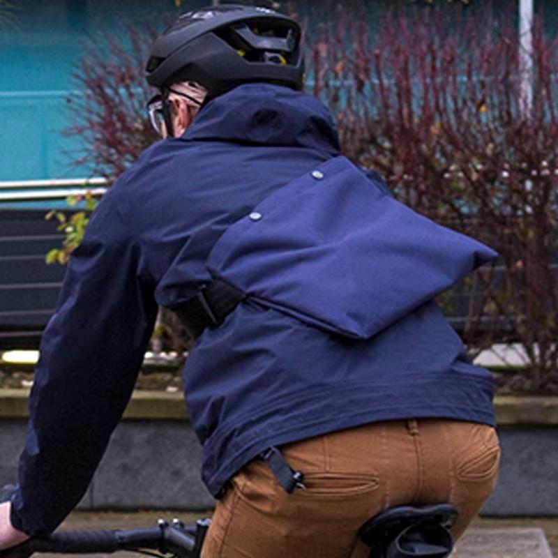 Cycling musette bag worn by a rider seen from behind on a bike ride, showing the bag on the back