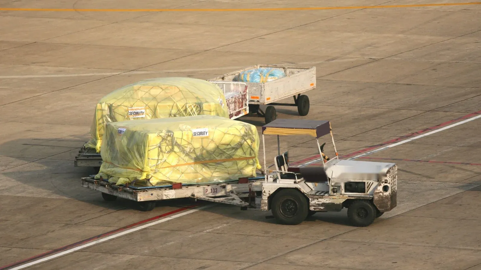 Netted, film-wrapped air cargo pallets towed across an airport apron in warm low sun