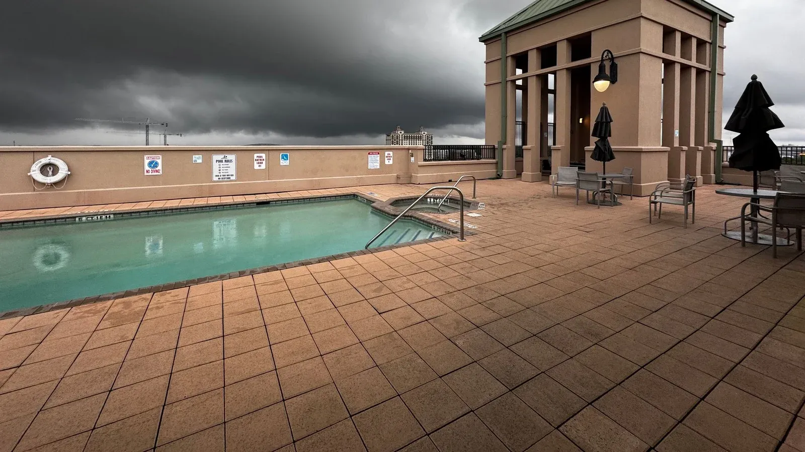 Rooftop pool under dark storm clouds, with a wide terracotta tile deck