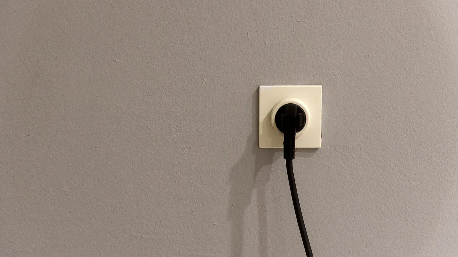 Black plug and cable in a wall socket on a plain grey wall