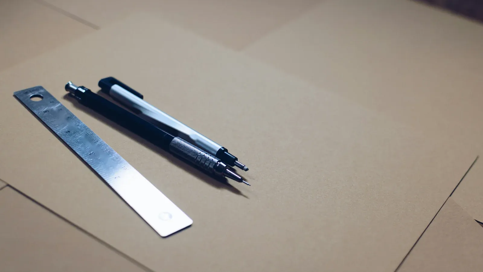 Kraft packaging board with a steel ruler and two pencils on a desk