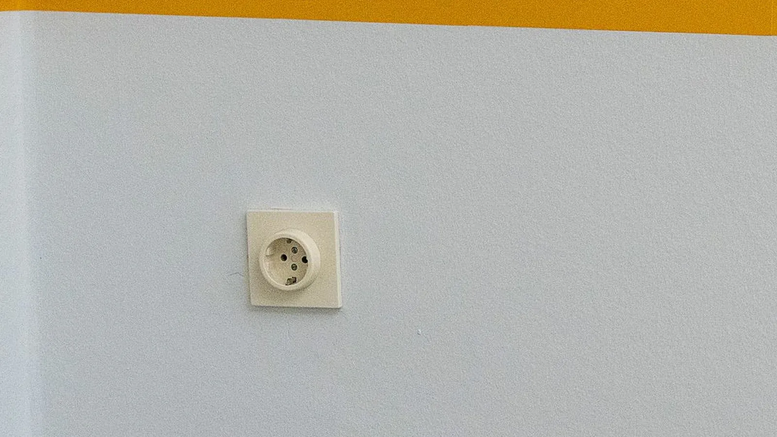 Wall socket on a plain white wall below a yellow stripe