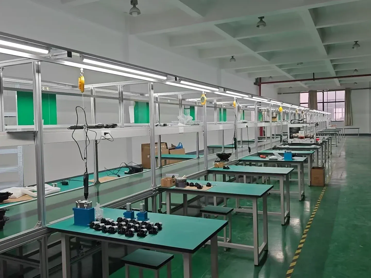 Empty pool robot assembly line with green ESD workbenches, hanging electric screwdrivers and motor parts