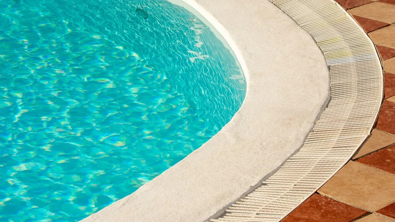 Curved pale stone pool edge with an overflow grate beside turquoise water