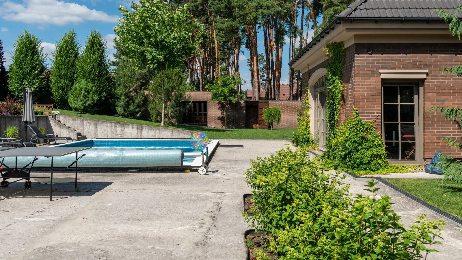 Backyard pool with a cover reel on a concrete deck beside a brick house