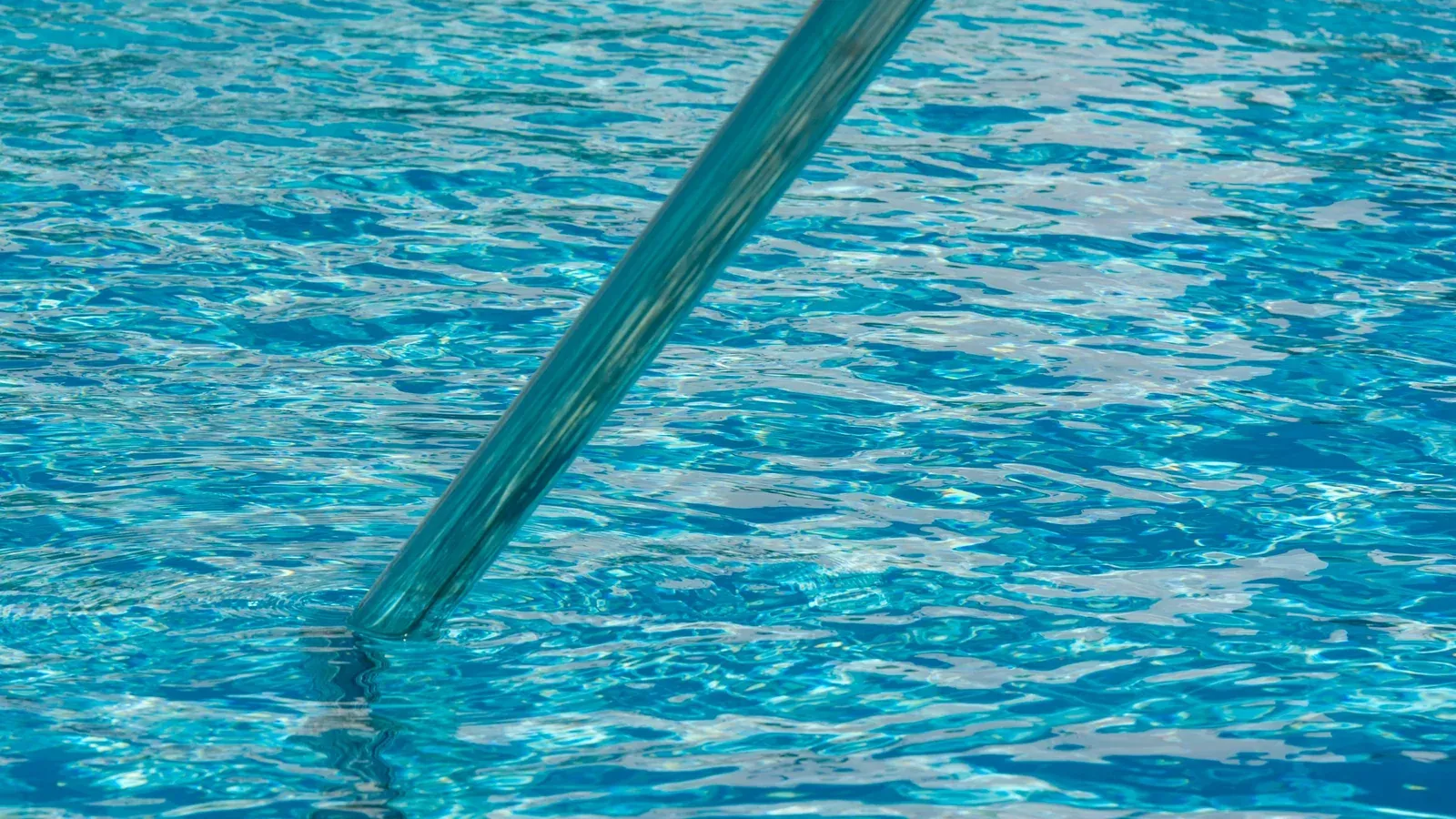 A pole dipping into clear blue pool water on a sunny day