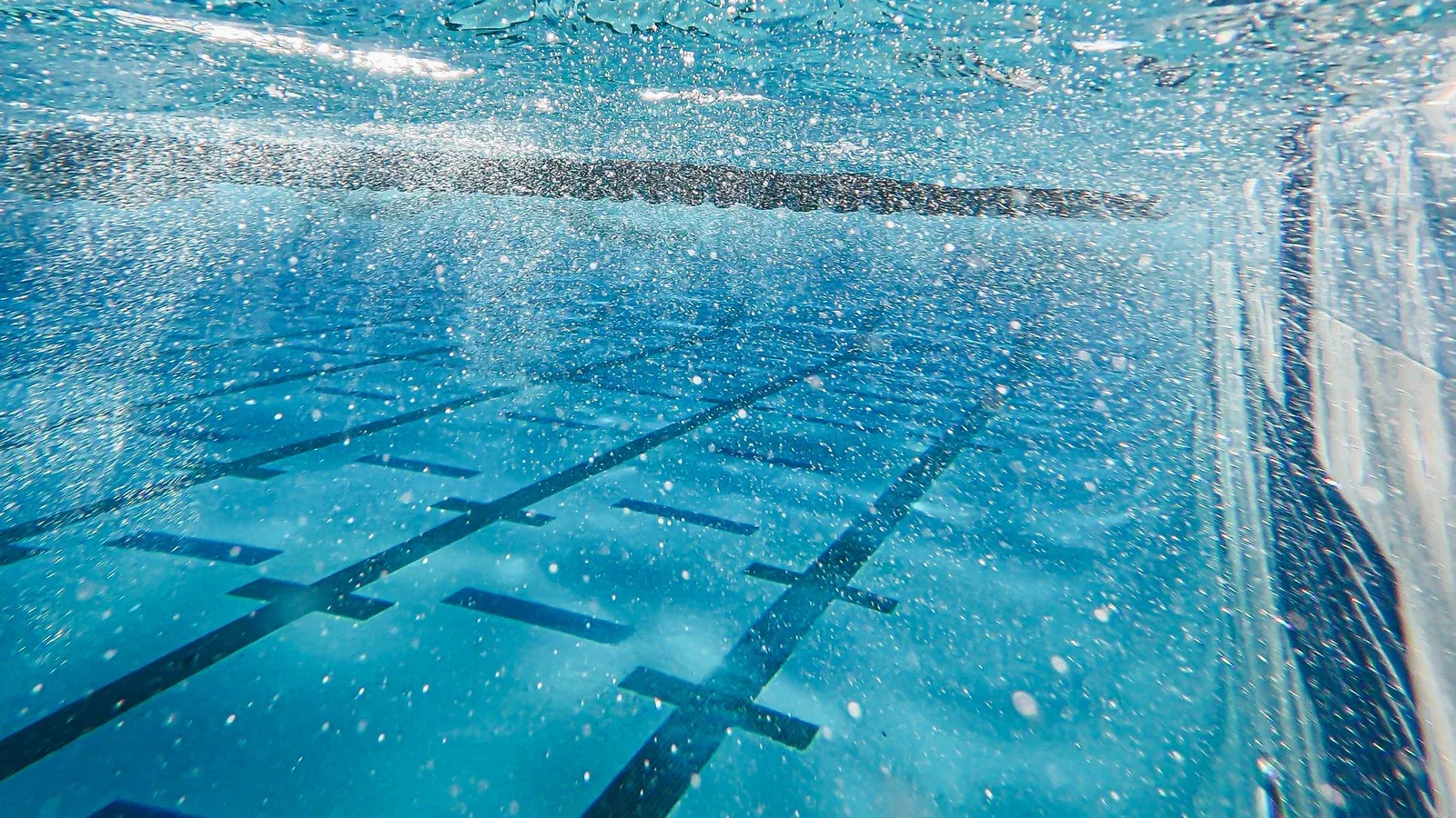 Underwater view along a pool floor with lane markings to where it meets the side wall