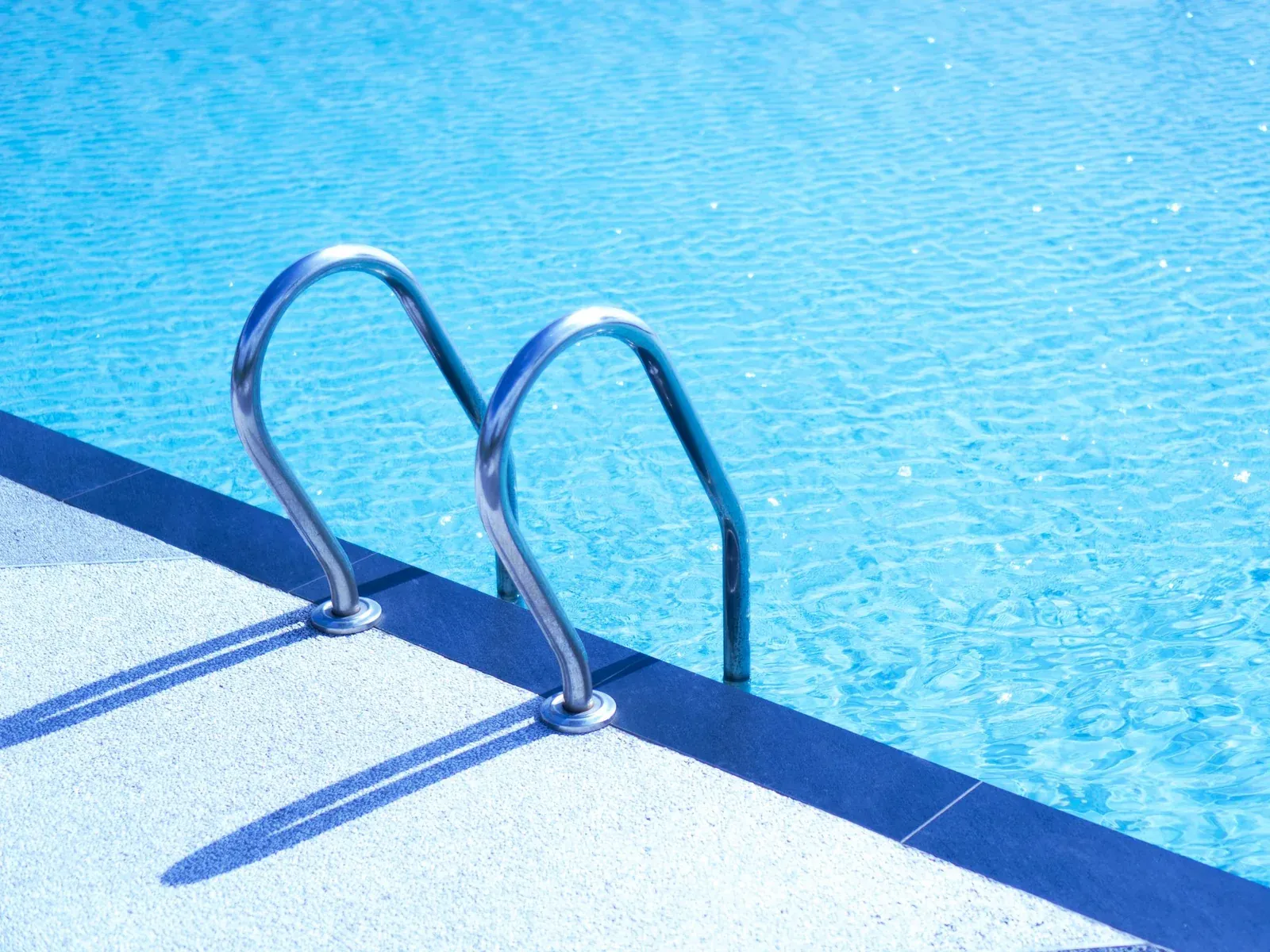 Stainless-steel pool ladder going down into clear water at the deep end, seen from the deck