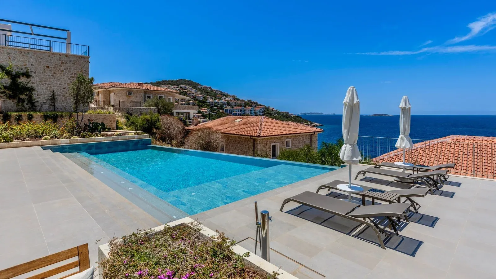 Infinity pool on a stone terrace above the sea, with sun loungers and closed parasols