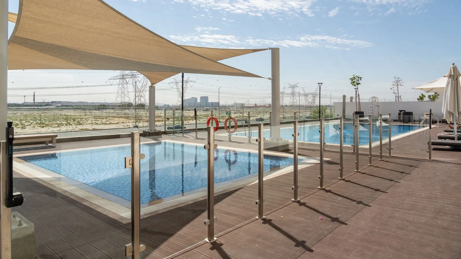 Pool behind a frameless glass fence with shade sails over the deck
