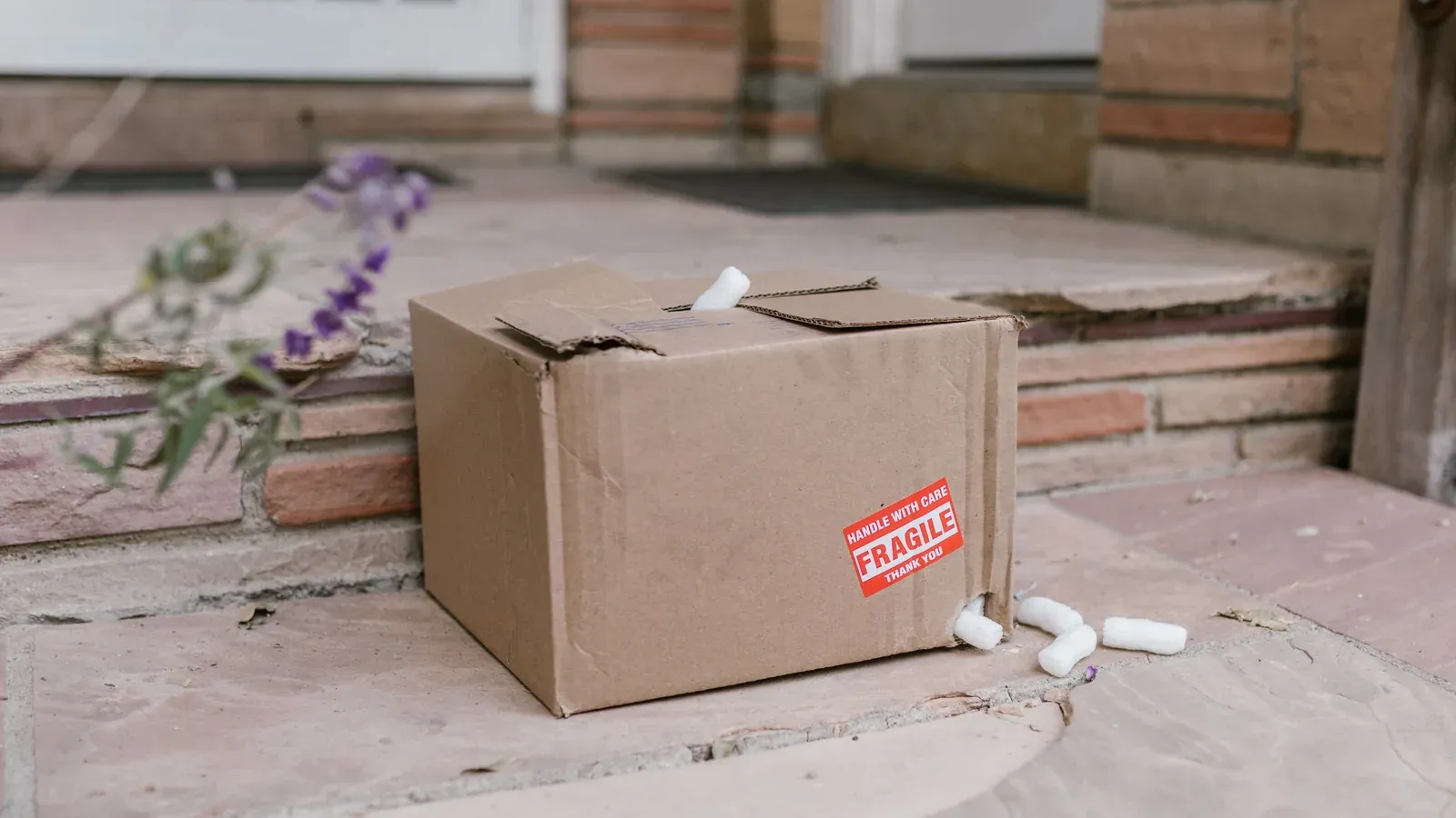 Battered brown carton with a crushed top and packing peanuts spilling out on a doorstep