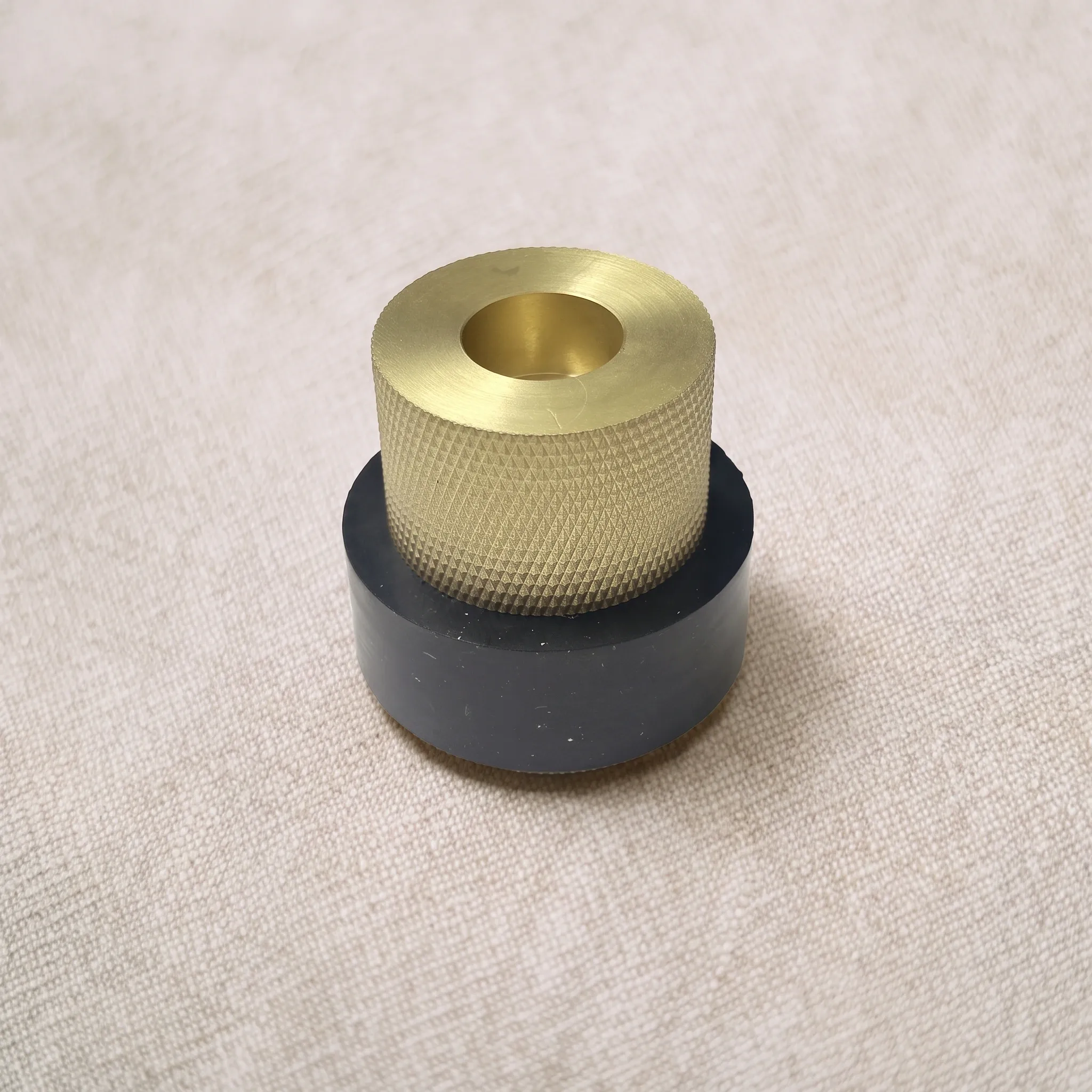 High angled view of the Brass Gold knurled door stop showing its tiered body, smooth black waist, and recessed top face on a neutral studio surface.