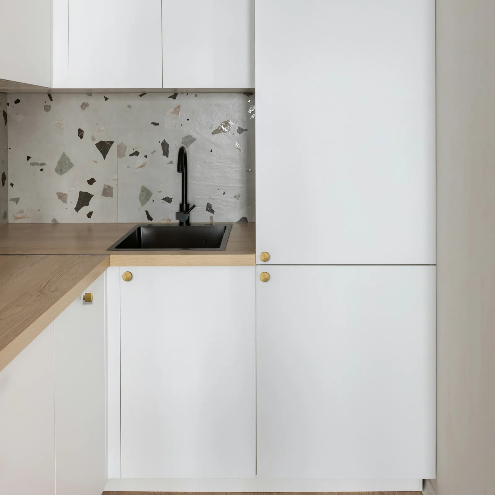 Brush Gold textured round aluminum knobs fitted on the white cabinet doors of a modern kitchen sink run with a terrazzo splashback.