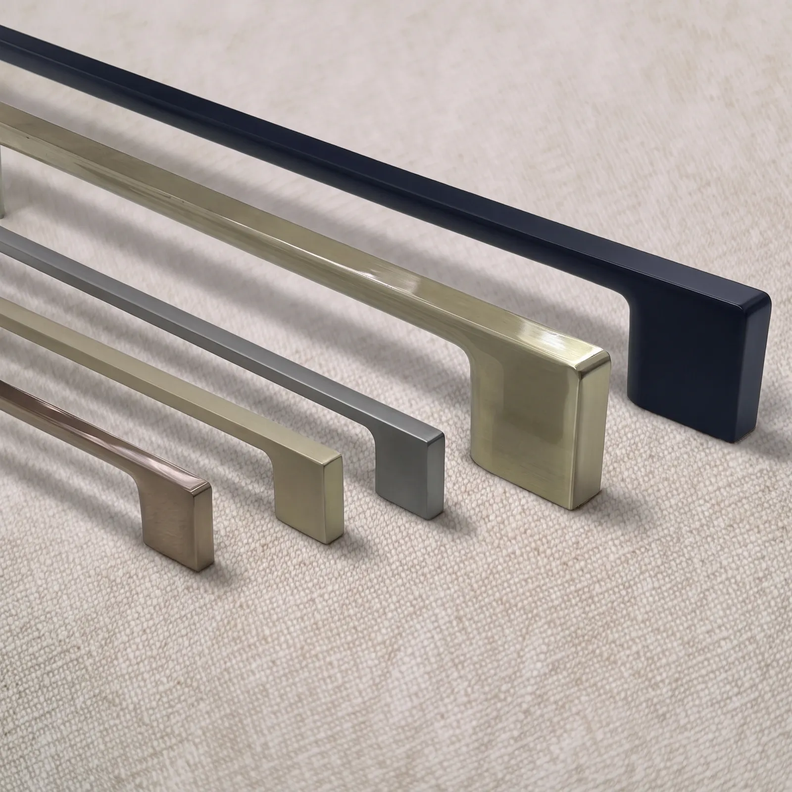 Group of D-profile zinc alloy bar pulls in assorted finishes with straight bars and flared feet on natural linen