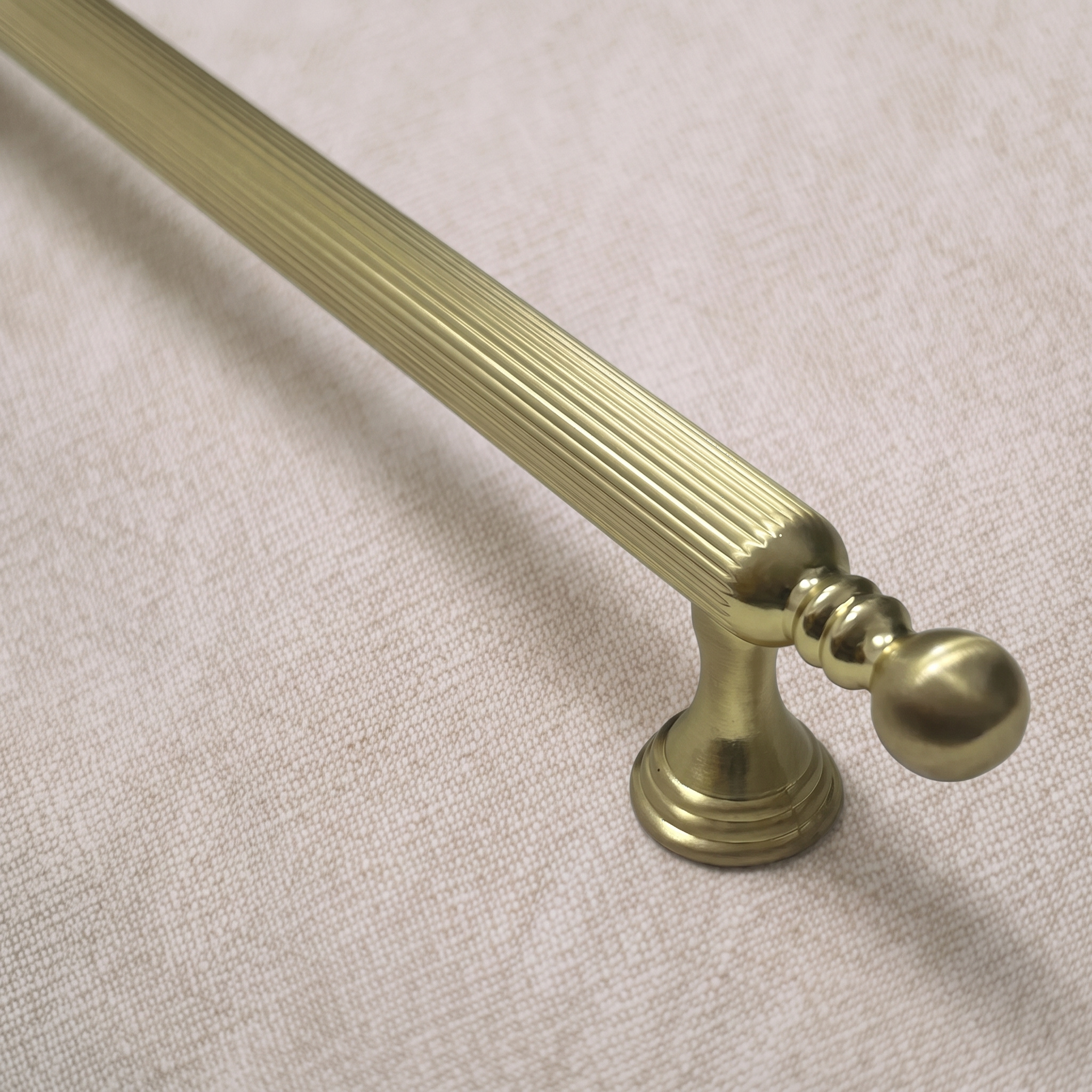 Close view of the ball terminal and paired ring collars at the end of the straight-grain zinc bar pull in Brass Gold