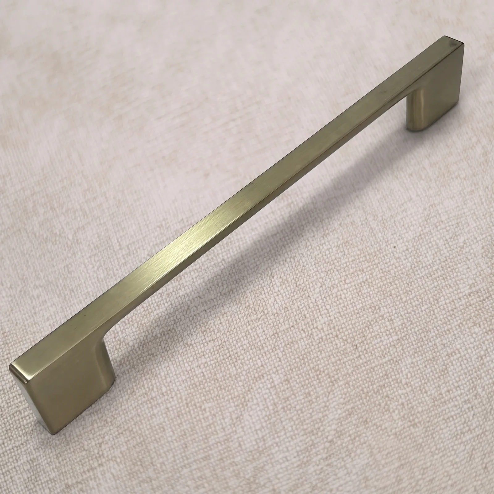 Angled view of a Brush Gold D-profile zinc alloy bar pull with a straight flat bar and flared feet on natural linen