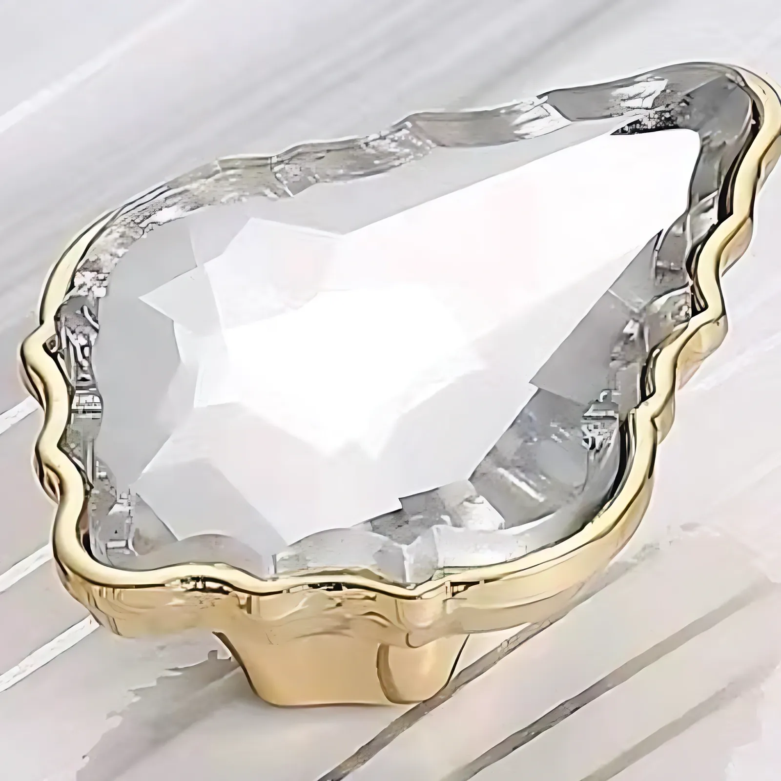 Angled view of one pear-shaped faceted clear crystal set inside a scalloped gold-tone frame knob, standing on white painted wood.