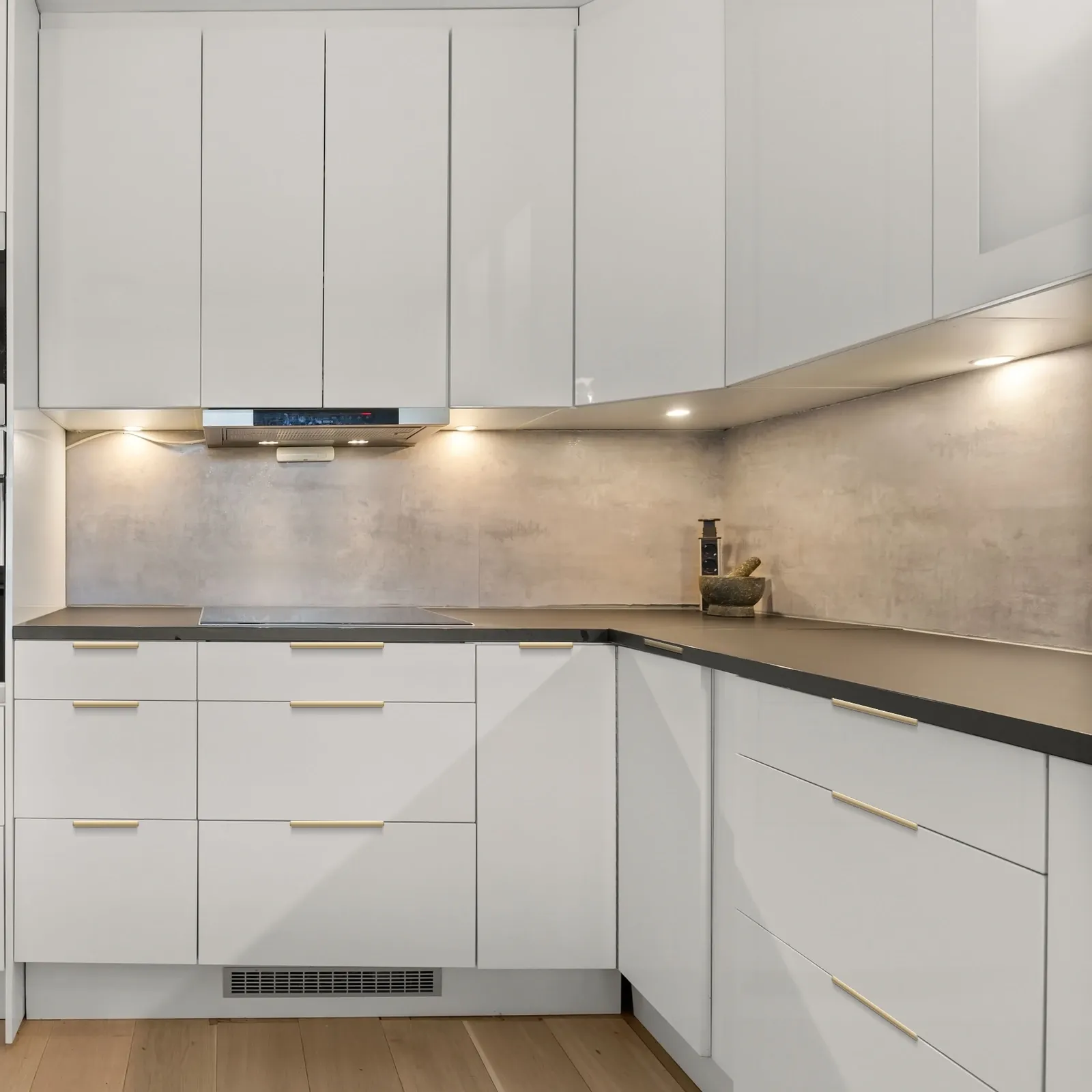 Champagne gold smooth-arc edge pulls installed across white kitchen drawer fronts and cabinet doors, including an L-shaped corner return.