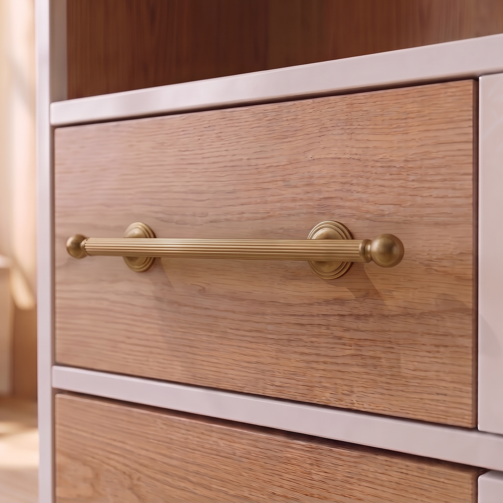 Straight-grain zinc cabinet pull in Brass Gold mounted horizontally on a light oak drawer front inside a white-framed cabinet, with ball terminals and paired ring collars in view