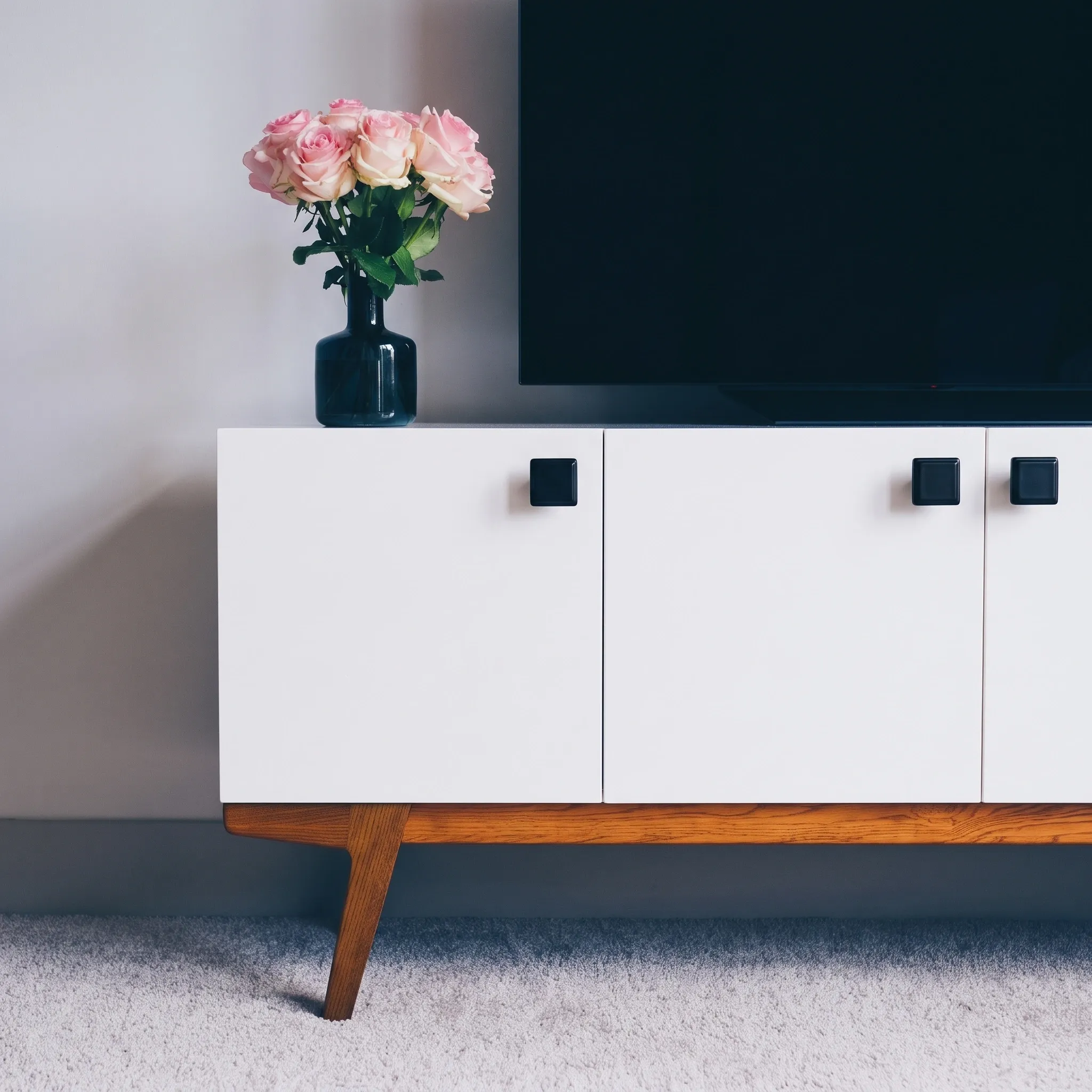 Interior scene showing Matt Black square knobs mounted on a white sideboard with a wood base beside pink roses and a dark television.