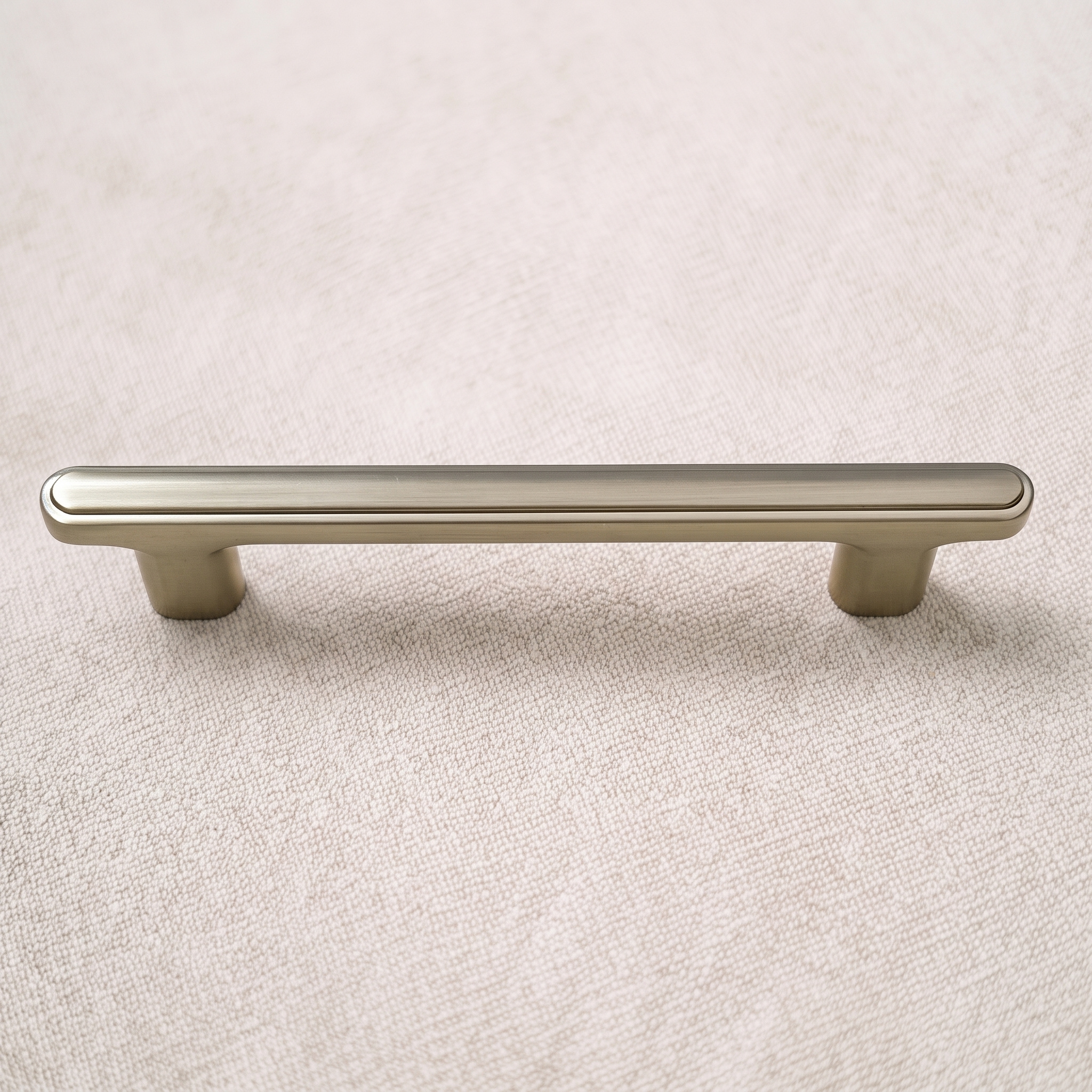 Brush Gold ridge-top bridge cabinet pull viewed straight on above a pale linen surface